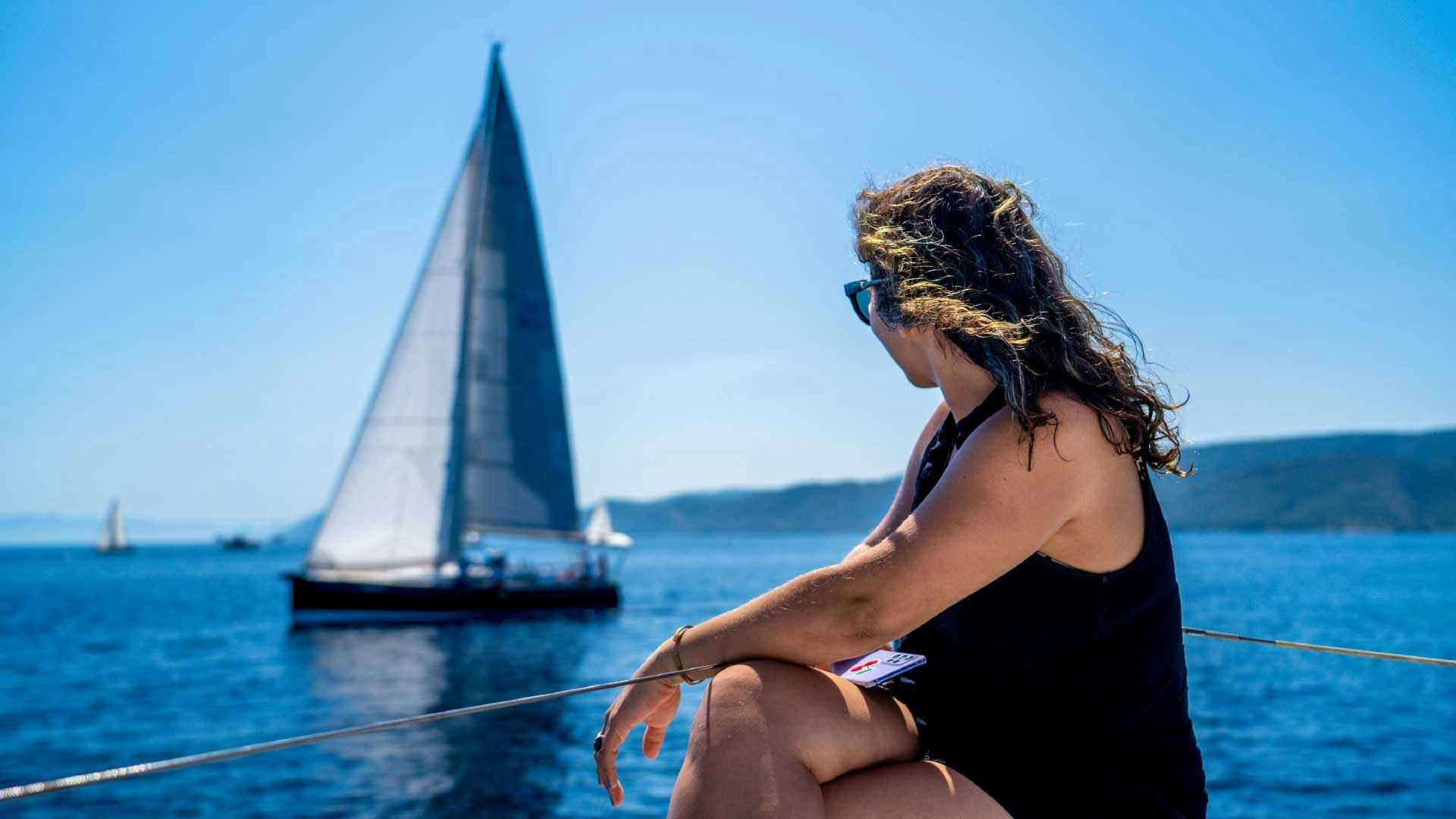 Woman sitting on bow of a catamaran looking at another yacht