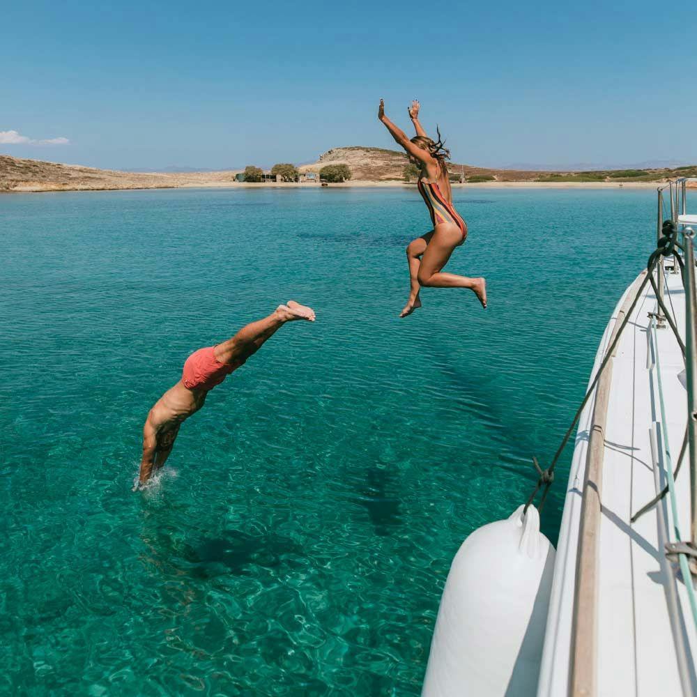 Two people jumping off a yacht into the sea in Greece