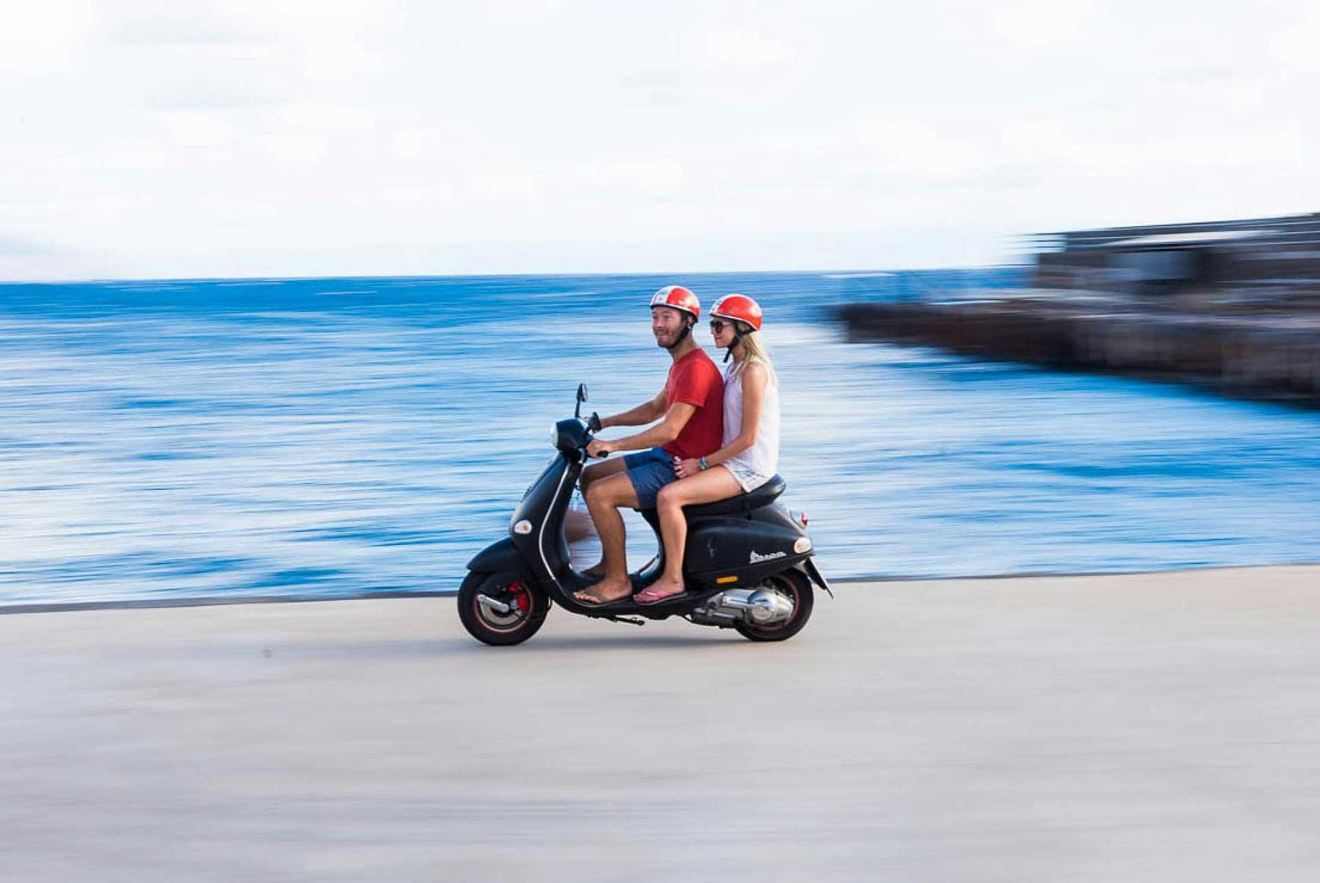 Couple riding on a scooter by the sea in Sicily
